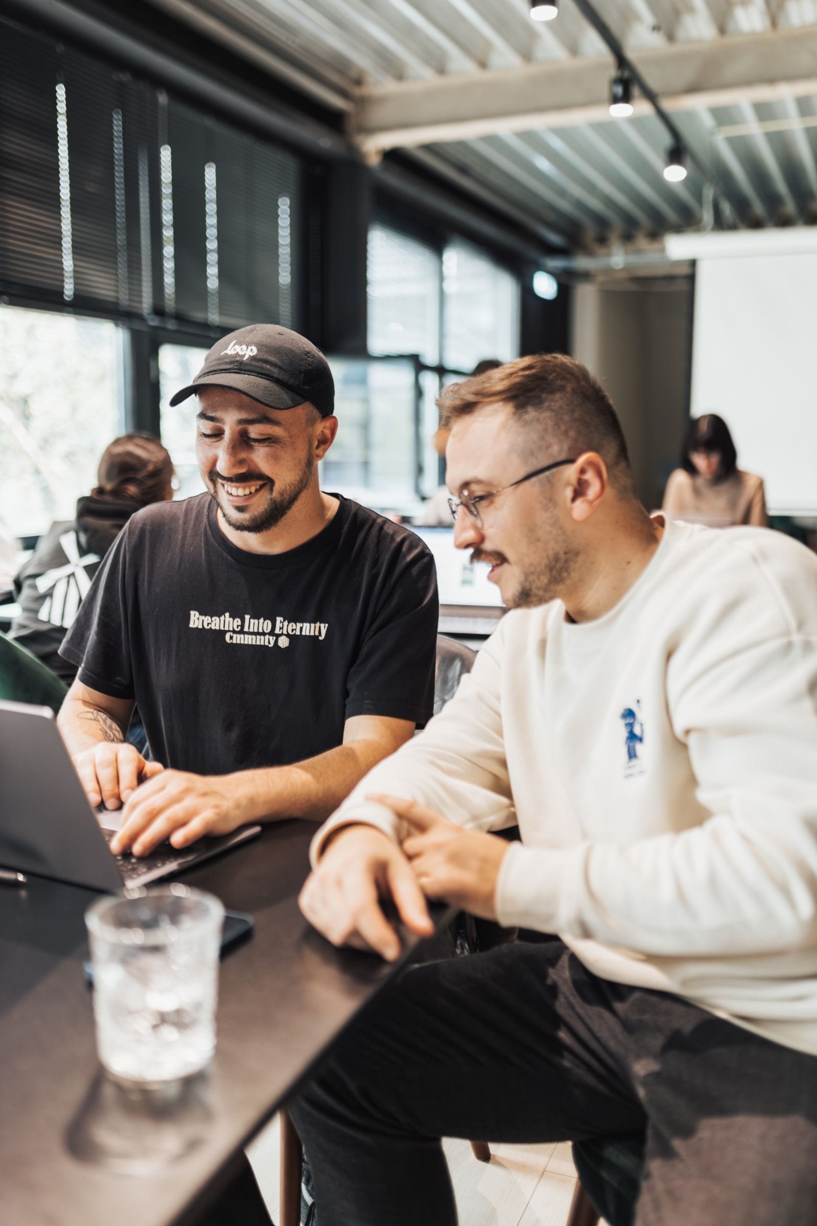 Two engineers laughing over their laptops at a shared desk