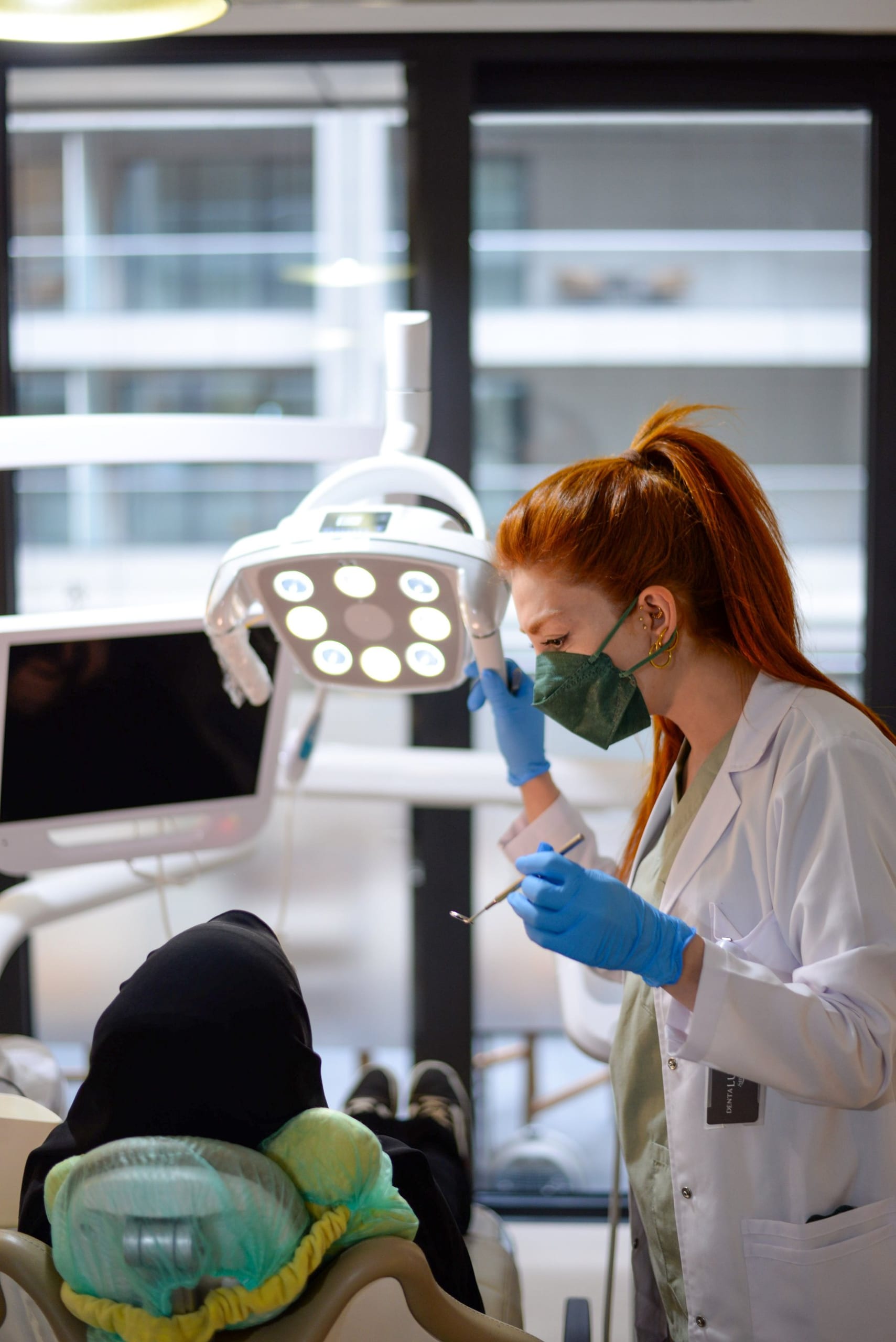 A dentist adjusting the light over a patient in a bright clinic