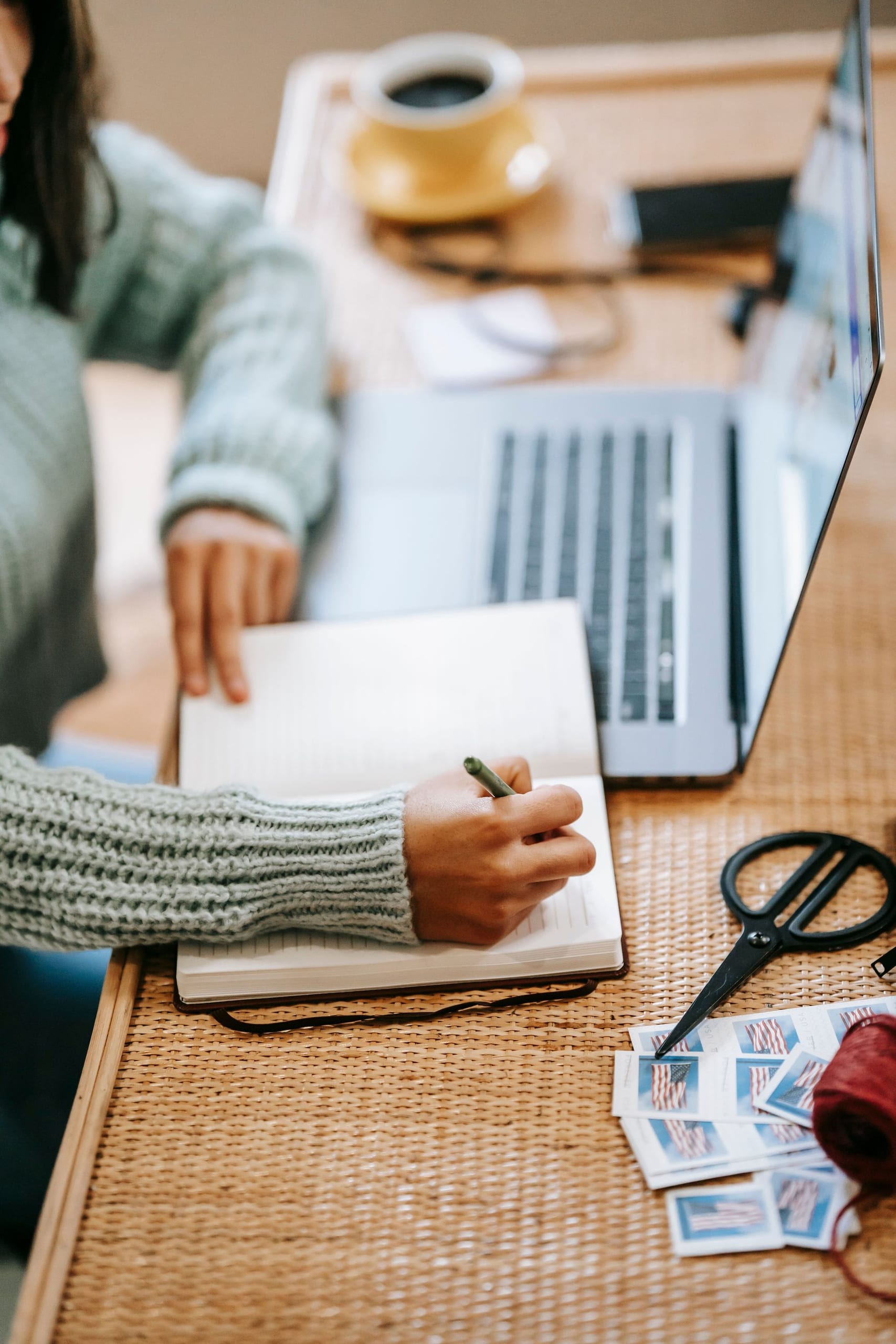 Writing in a notebook beside a laptop on a wooden desk