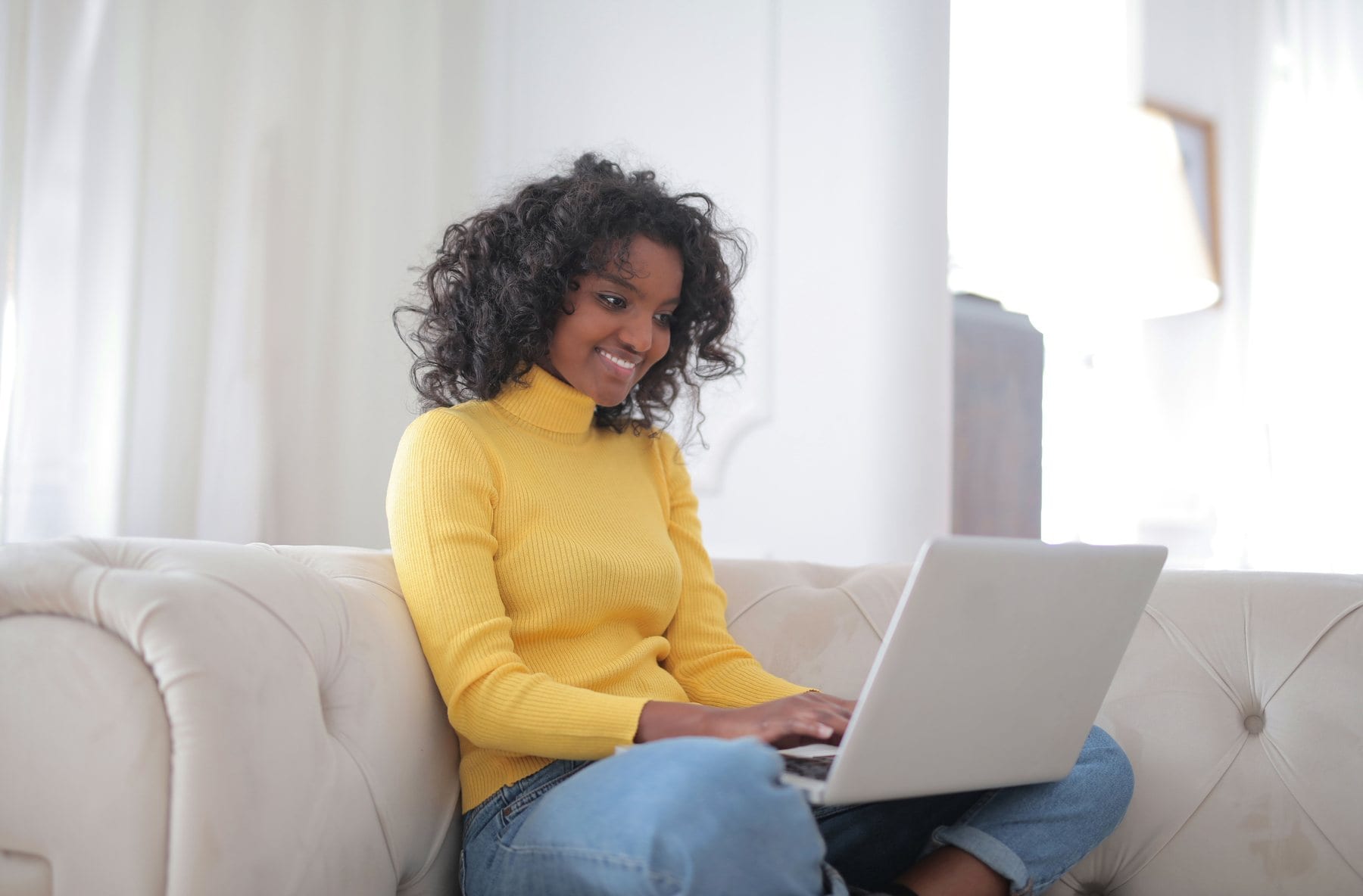 A young woman smiling at her laptop on a sofa