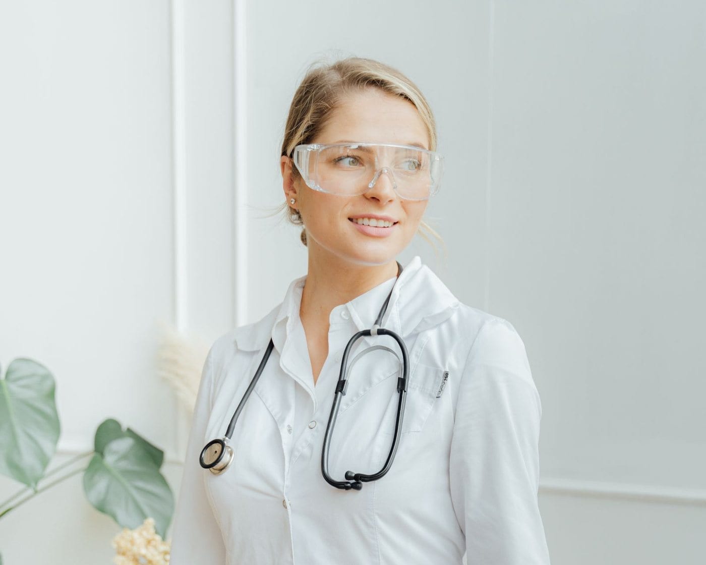 A physician in a white coat and safety glasses with a stethoscope