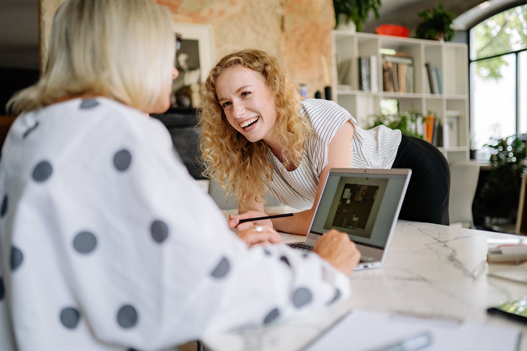 Two colleagues laughing together over a laptop at the office