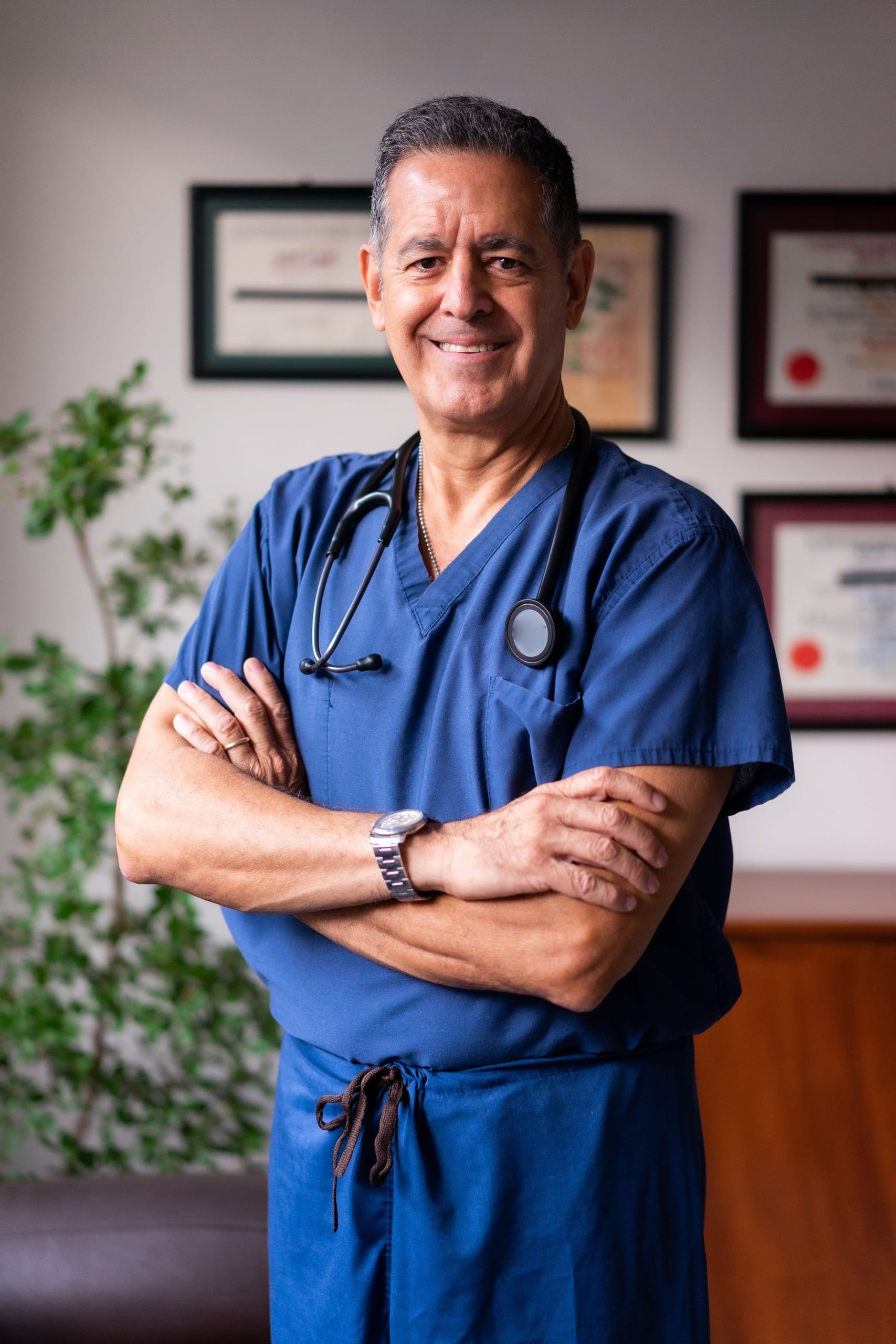 A smiling clinician in blue scrubs in his office