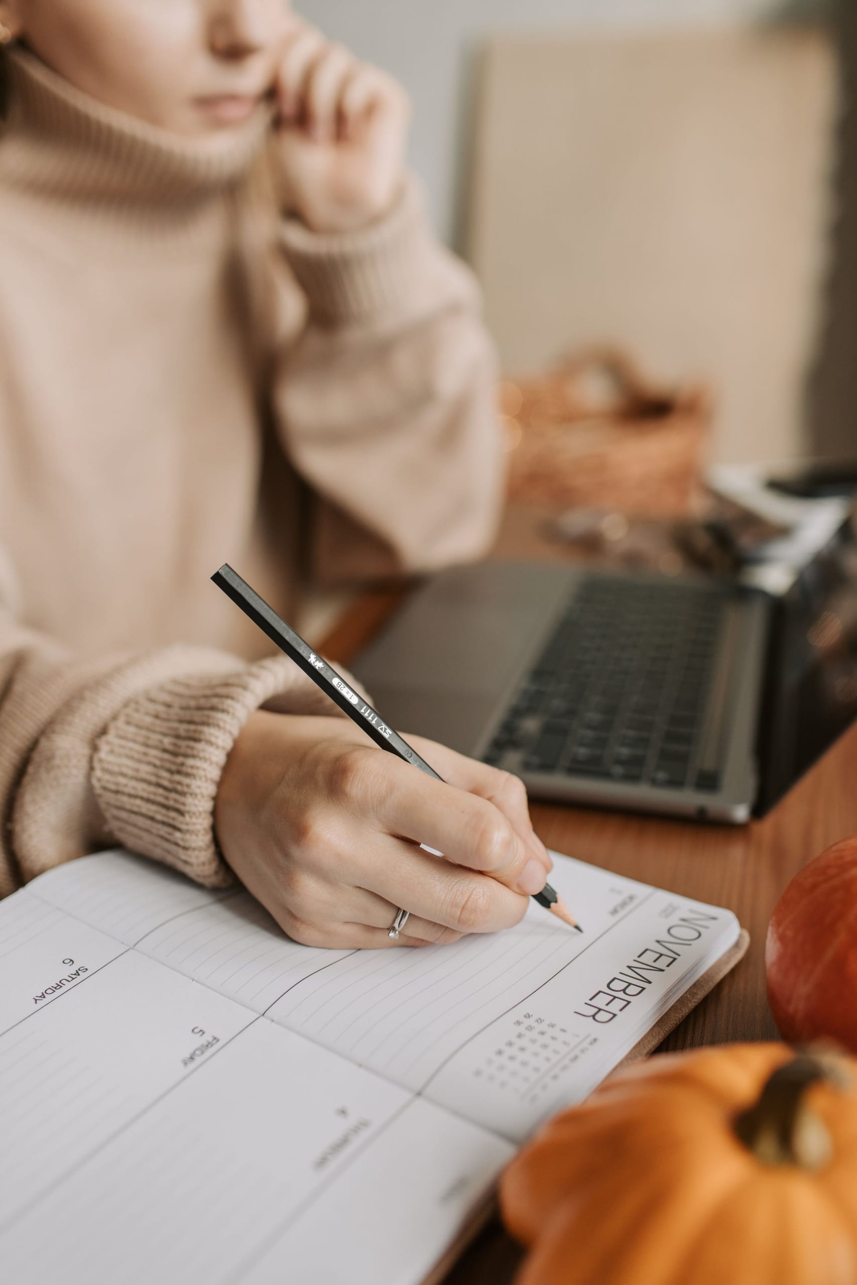 Writing in a planner beside a laptop at a warm desk
