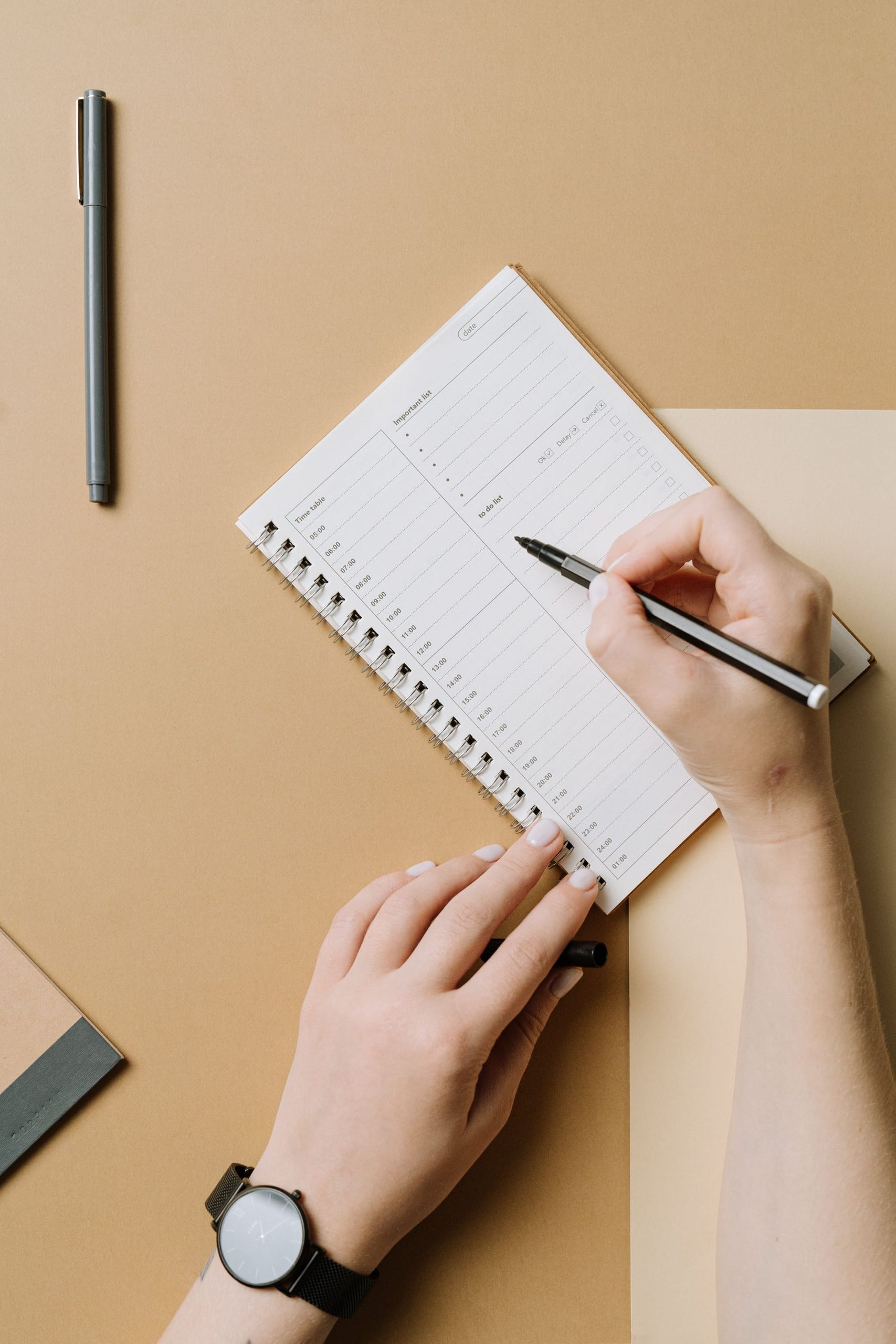 Hands writing in a weekly planner on a tan desk