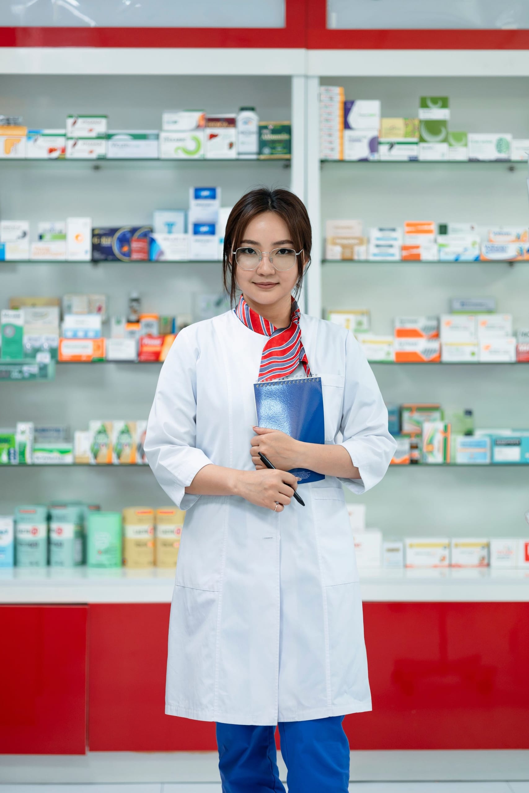 A pharmacist in a white coat in front of pharmacy shelves