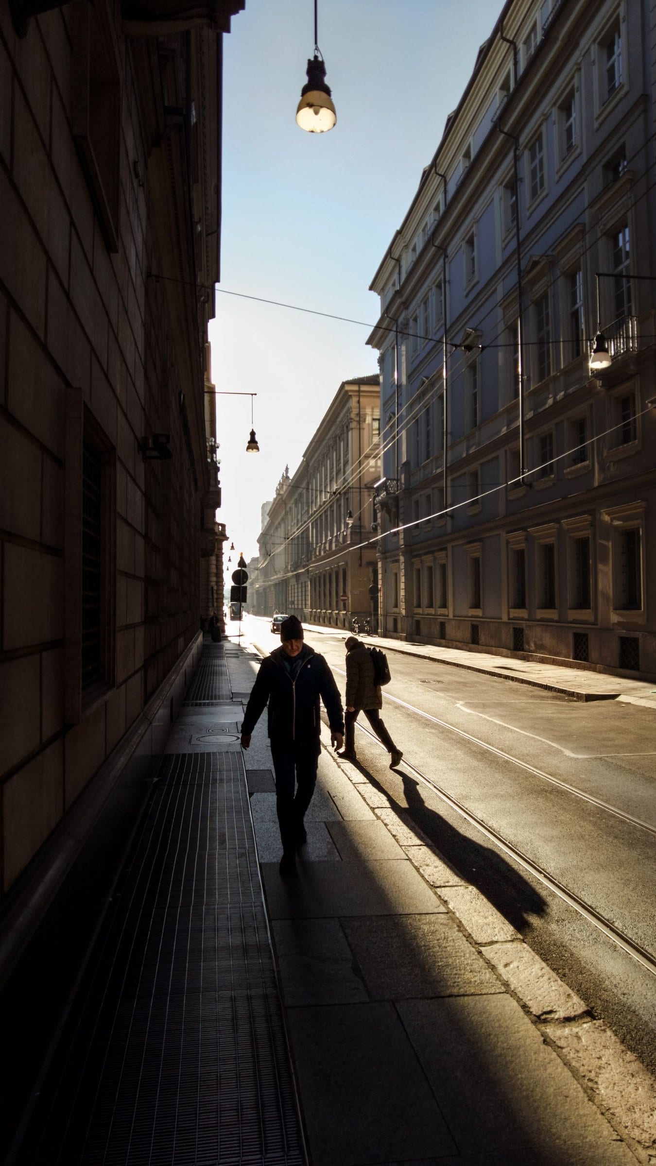 People walking down a sunlit city street in the morning