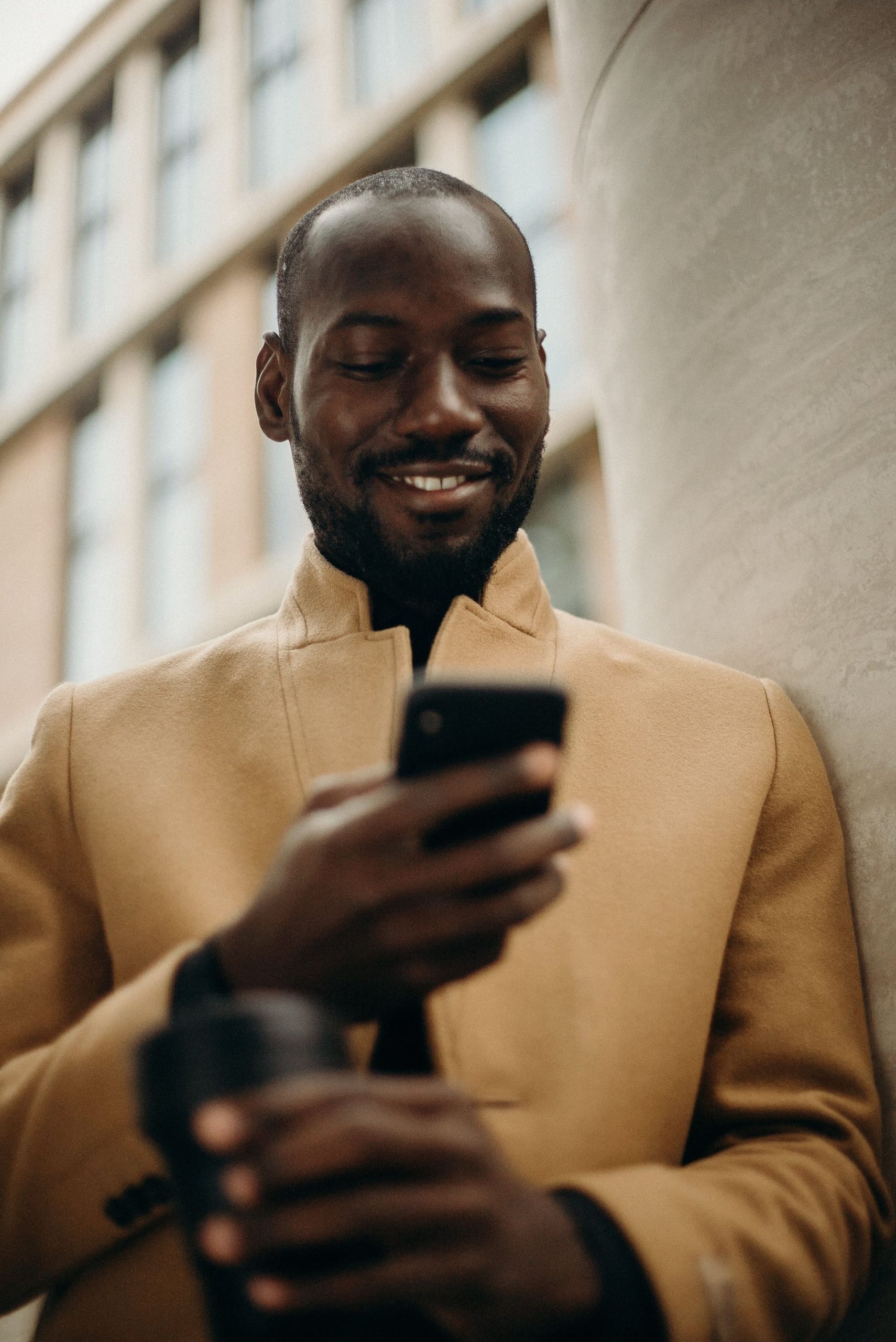 A young professional smiling at his phone on a city street